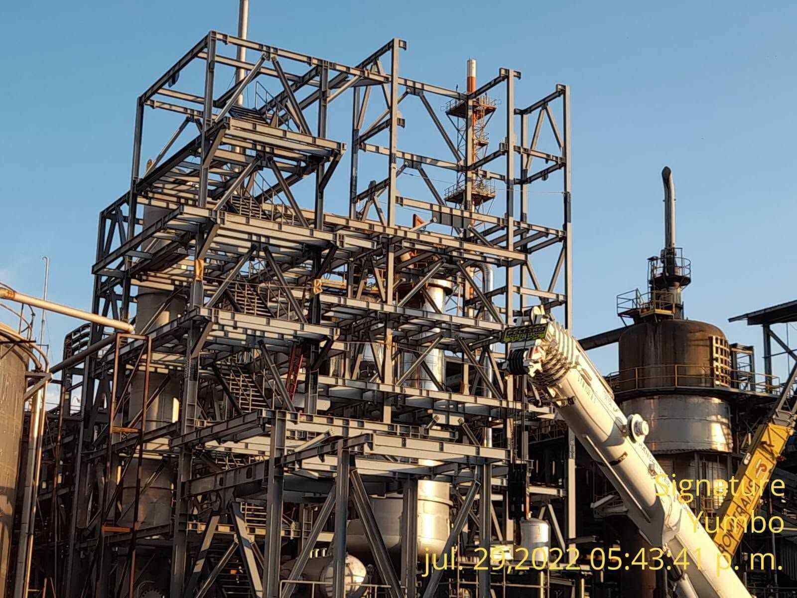 Erected steel frame on site with braced bays, platforms, stairs, and structural members.